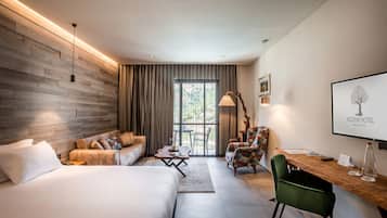Quarto de hotel moderno com parede de madeira, uma cama grande, um sofá, uma escrivaninha com cadeira e vista para o exterior.