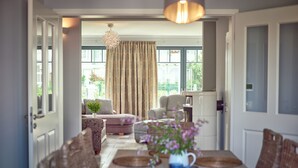 A dining area with a table set for four, a chandelier, and a view of the garden through large windows. - VILLA EMMA 4A- luxury with sauna, whirlpool, fireplace, view, for 8 pers.+ Babybet (Sellin)