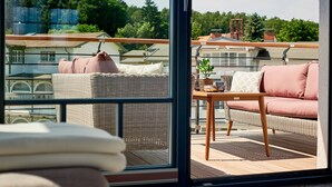 A balcony with wicker furniture, a cushioned sofa, and a small table with a plant. - VILLA EMMA 4A- luxury with sauna, whirlpool, fireplace, view, for 8 pers.+ Babybet (Sellin)
