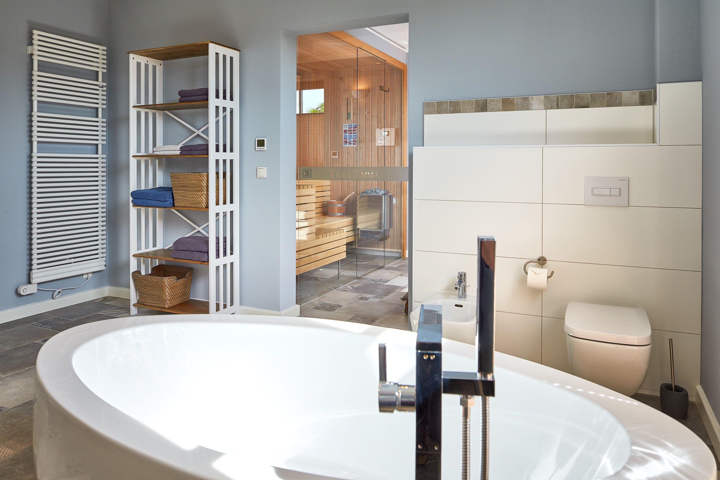 Ein modernes Badezimmer mit einer freistehenden Badewanne, einem weißen Heizkörper und einer Holzregaleinrichtung.