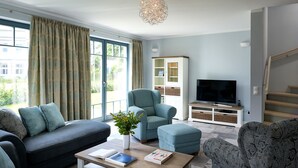 A modern living room with a sofa, ottoman, and armchair, a television, and a cabinet with glass doors. - VILLA EMMA 4A- luxury with sauna, whirlpool, fireplace, view, for 8 pers.+ Babybet (Sellin)