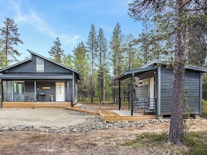 A cabin with a deck, a covered porch, and a small shed in a forested area.