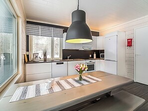 A modern kitchen with a central island, white cabinetry, a black pendant light, and a window with blinds. - Pallaskieppi by Interhome (Raattama)