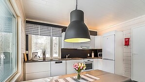 Una cocina moderna con una isla central, armarios blancos, una lámpara colgante negra y un ventanal con persianas.