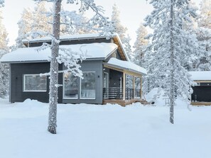 A cabin with a covered porch and large windows, surrounded by snow-covered trees. - Pallaskieppi by Interhome (Raattama)