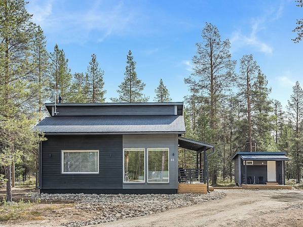 A modern cabin with a large window, a covered porch, and a small adjacent structure.