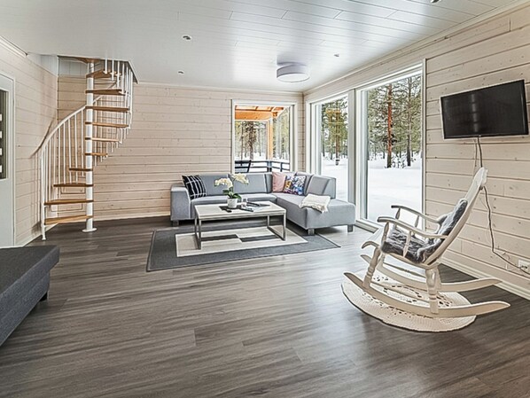 A spacious living room with a wooden staircase, a grey sofa, a coffee table, and a rocking chair. - Pallaskieppi by Interhome (Raattama)