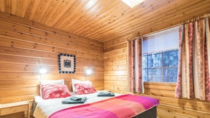 Une chambre à coucher dans une cabane en bois, avec un lit, deux tables de chevet, une fenêtre avec des rideaux et un tableau encadré au mur.