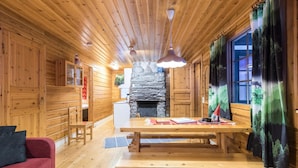 L’intérieur d’un chalet en bois, avec une cheminée en pierre, une table à manger en bois et un canapé rouge.