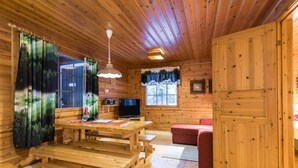 L’intérieur d’un chalet en bois comprend une table à manger en bois, un canapé rouge, un téléviseur et une fenêtre avec des rideaux.