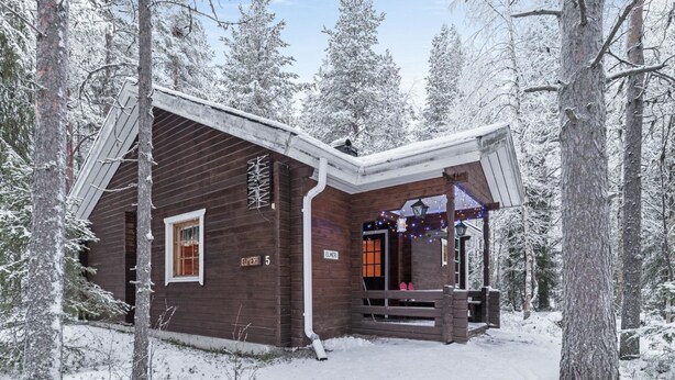 Une cabane en bois dotée d’un porche abrité, entourée d’arbres couverts de neige.