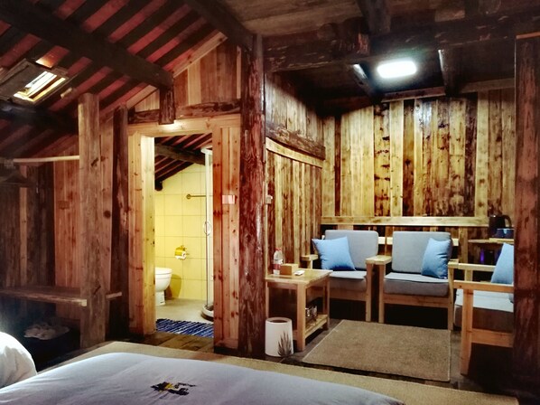 A rustic wooden room with a bed, a small table, and two chairs. There is a bathroom visible through an open doorway. - Lost World Sanjiang (Liuzhou)