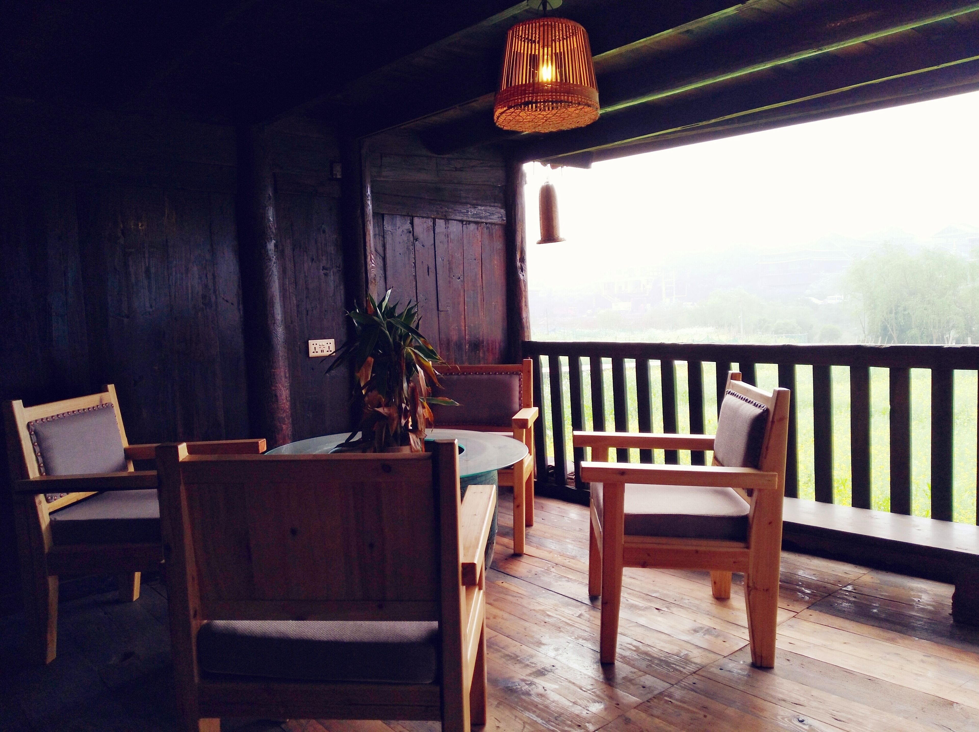 A wooden interior with a table and chairs, a hanging light fixture, and a view through a window.
