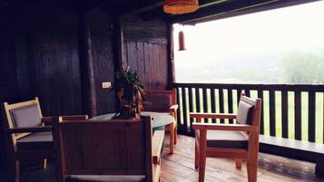 A wooden interior with a table and chairs, a hanging light fixture, and a view through a window.