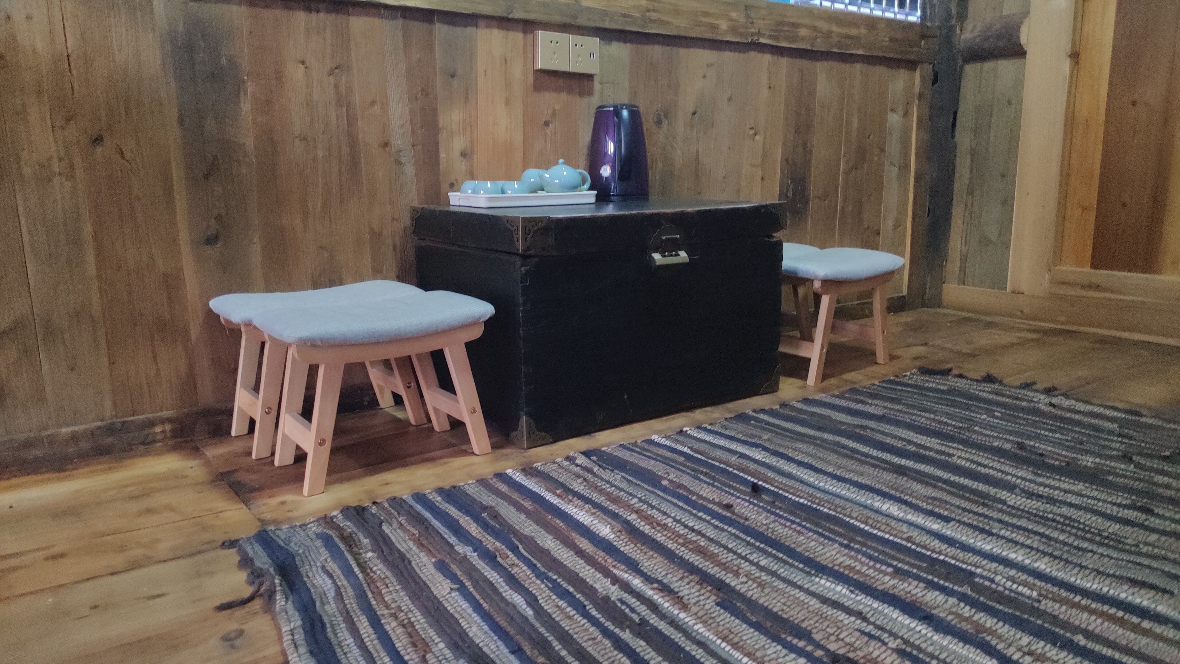 Une pièce en bois avec une commode noire, deux tabourets roses et un tapis à rayures.
