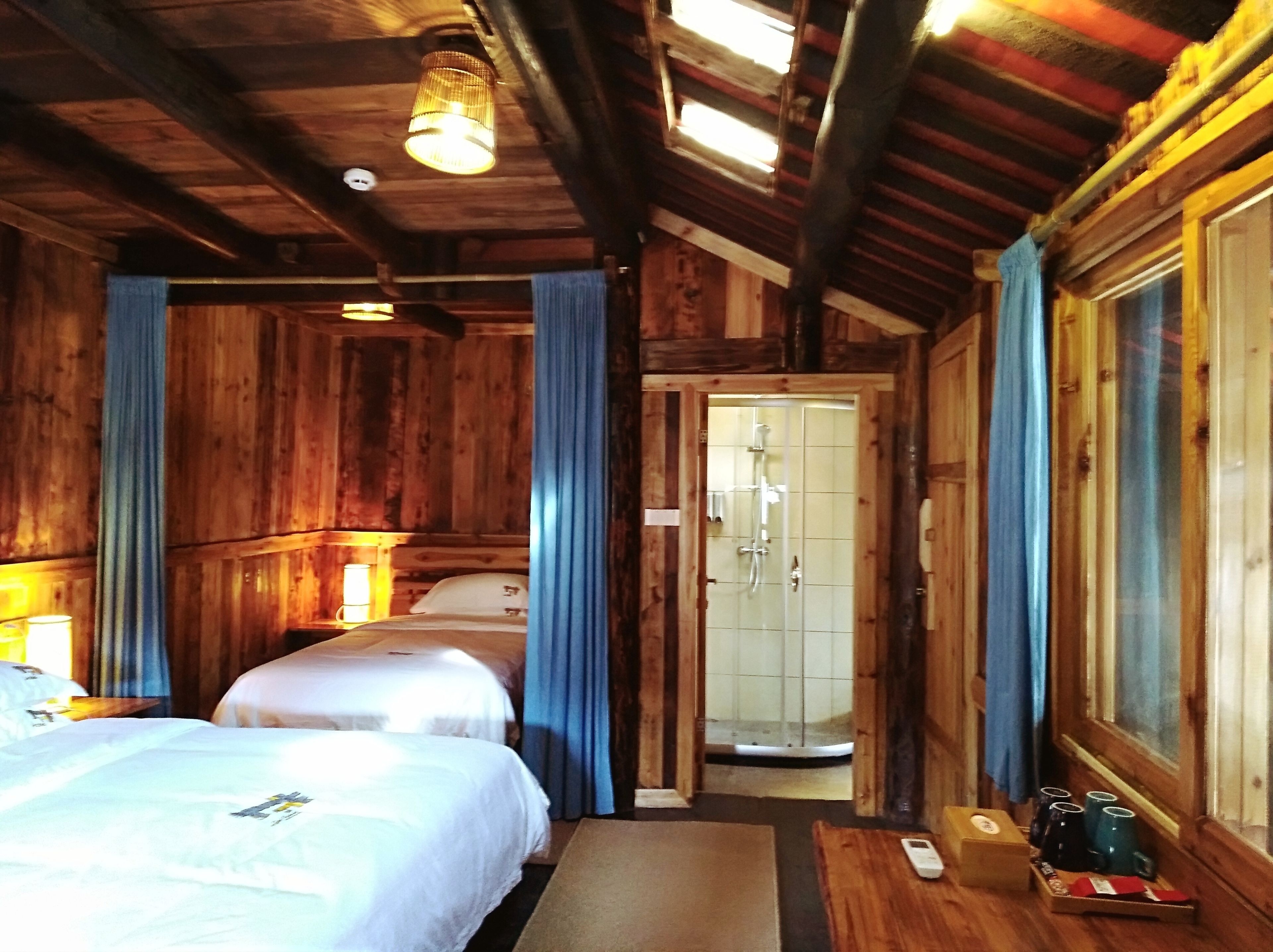 Una habitación de cabaña de madera con dos camas, ducha y una mesita con tazas.