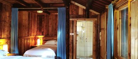 Una habitación de cabaña de madera con dos camas, ducha y una mesita con tazas.