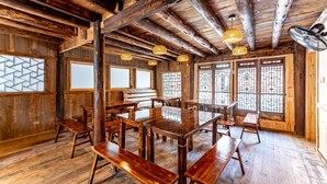 Un interior de madera con una gran mesa de comedor rodeada de bancos, vigas de madera en el techo y ventanas tradicionales con diseños de celosía.