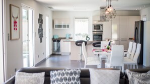 A modern kitchen with white cabinets, a dining area with white chairs, and a living room with a black and white sofa. - LA CORNICHE D'ARGENT VI4136 by RIVIERA HOLIDAY HOM (Niza)