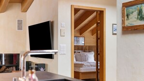 A cozy room with a bed, a television mounted on the wall, and a wooden ceiling. - Rütschi by Interhome (Zermatt)