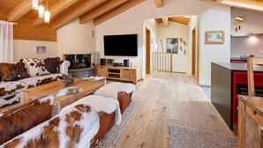 A cozy living room with a wooden ceiling, a fireplace, a TV, and a sofa with cowhide cushions. - Rütschi by Interhome (Zermatt)