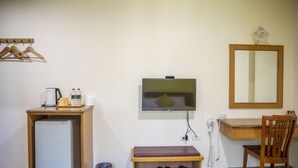 Habitación pequeña con escritorio, silla, televisión, refrigerador y espacio para zapatos.