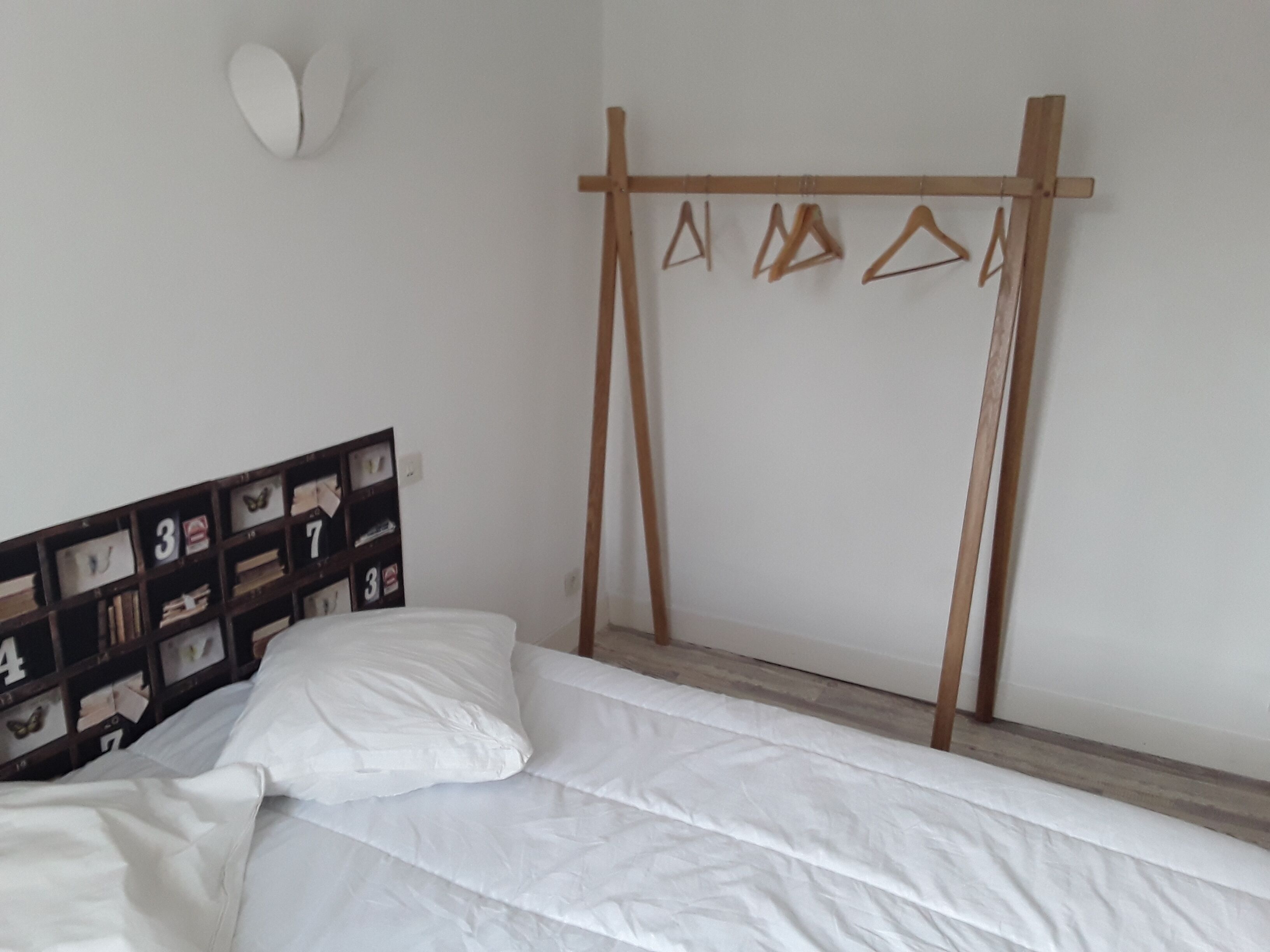 A bedroom with a bed, a wooden hanger rack, and a wall-mounted shelf with numbered compartments.