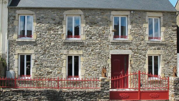 Un edificio de piedra con techo gris, varias ventanas y una verja roja.