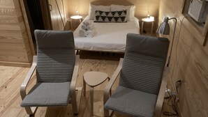 Et hyggeligt værelse med en seng, to lænestole, et lille bord og en fastmonteret varmeovn.