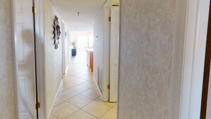 Un couloir avec des portes blanches, un sol carrelé et un luminaire au plafond.