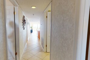 Un couloir avec des portes blanches, un sol carrelé et un luminaire au plafond.