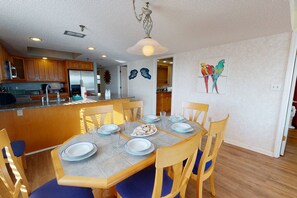 A dining area with a table set for four, wooden chairs, and a kitchen in the background.