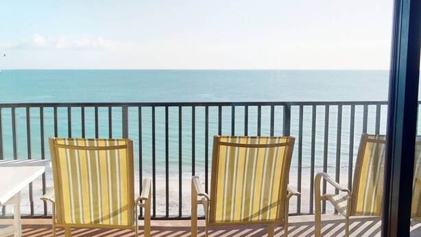 Un balcon avec trois chaises à rayures donnant sur une mer calme.