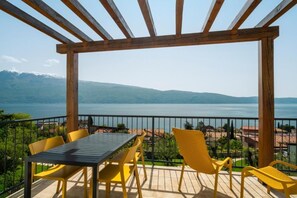 A wooden pergola with a table and chairs overlooking a lake and mountains. - Residence Dany (Gargnano)
