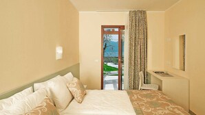 Habitación de hotel con cama, escritorio, silla, espejo y vista a un jardín a través de una puerta.