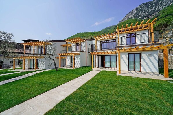 A modern two-story building with a covered outdoor area, a paved walkway, and a grassy lawn. - Residence Dany (Gargnano)