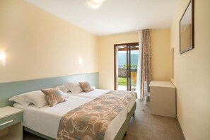A hotel room with a bed, a nightstand, a small table, and a view of the outdoors through a glass door. - Residence Dany (Gargnano)