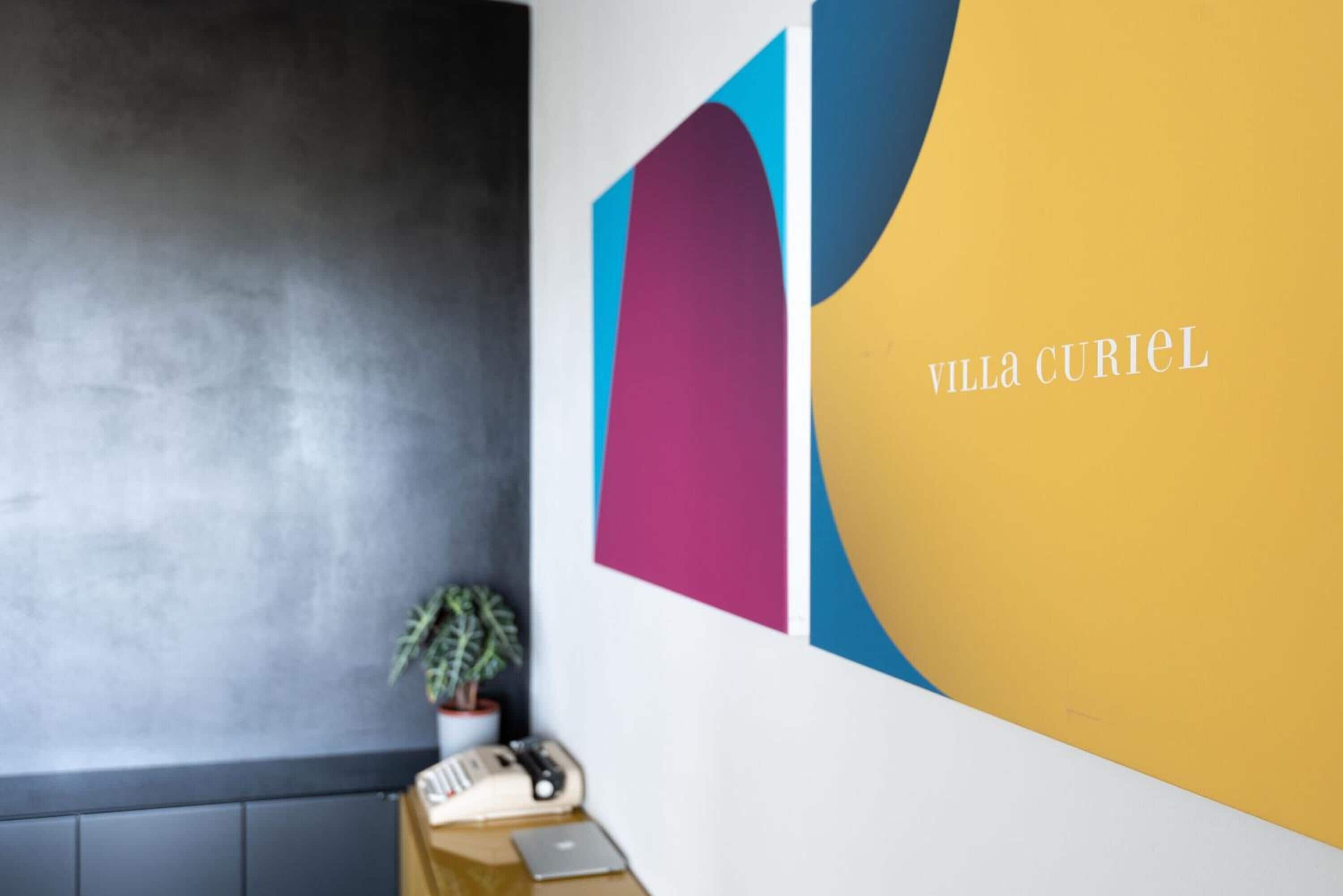 A room with a desk, a potted plant, and a wall with abstract art.