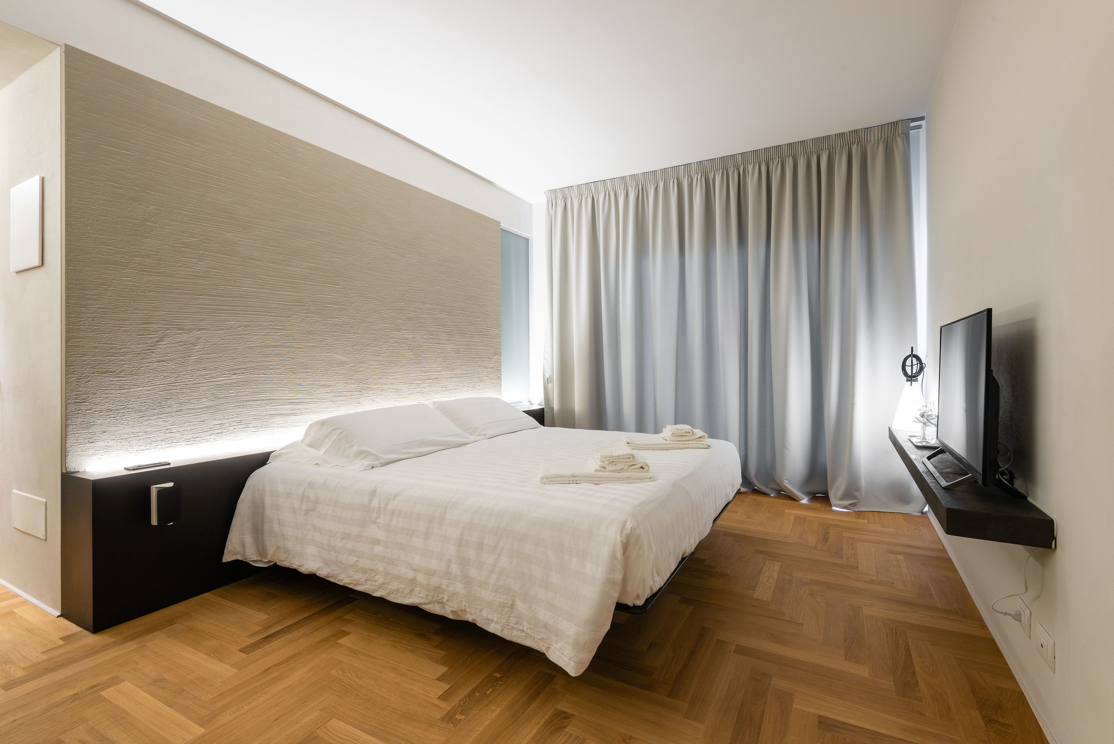Una camera da letto moderna con un letto, una televisione e una finestra con tende.