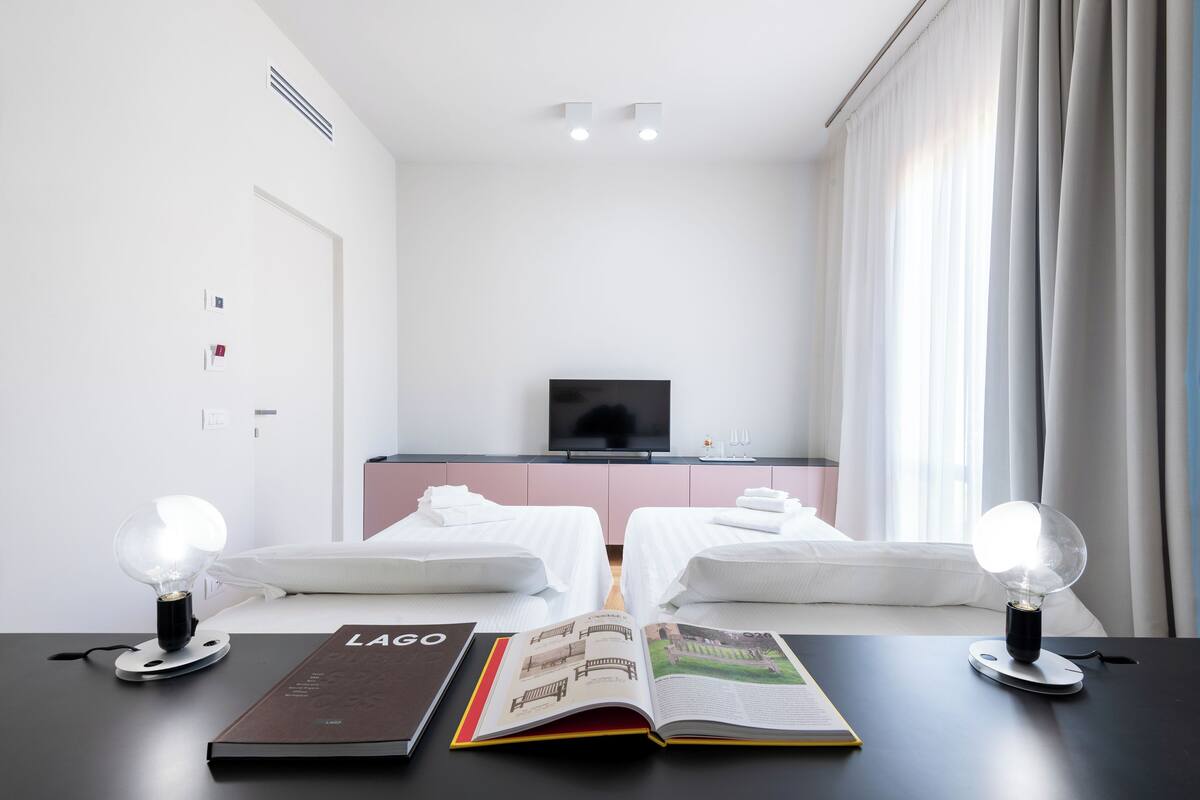 A hotel room with two beds, a TV, and a table with a book and a lamp.