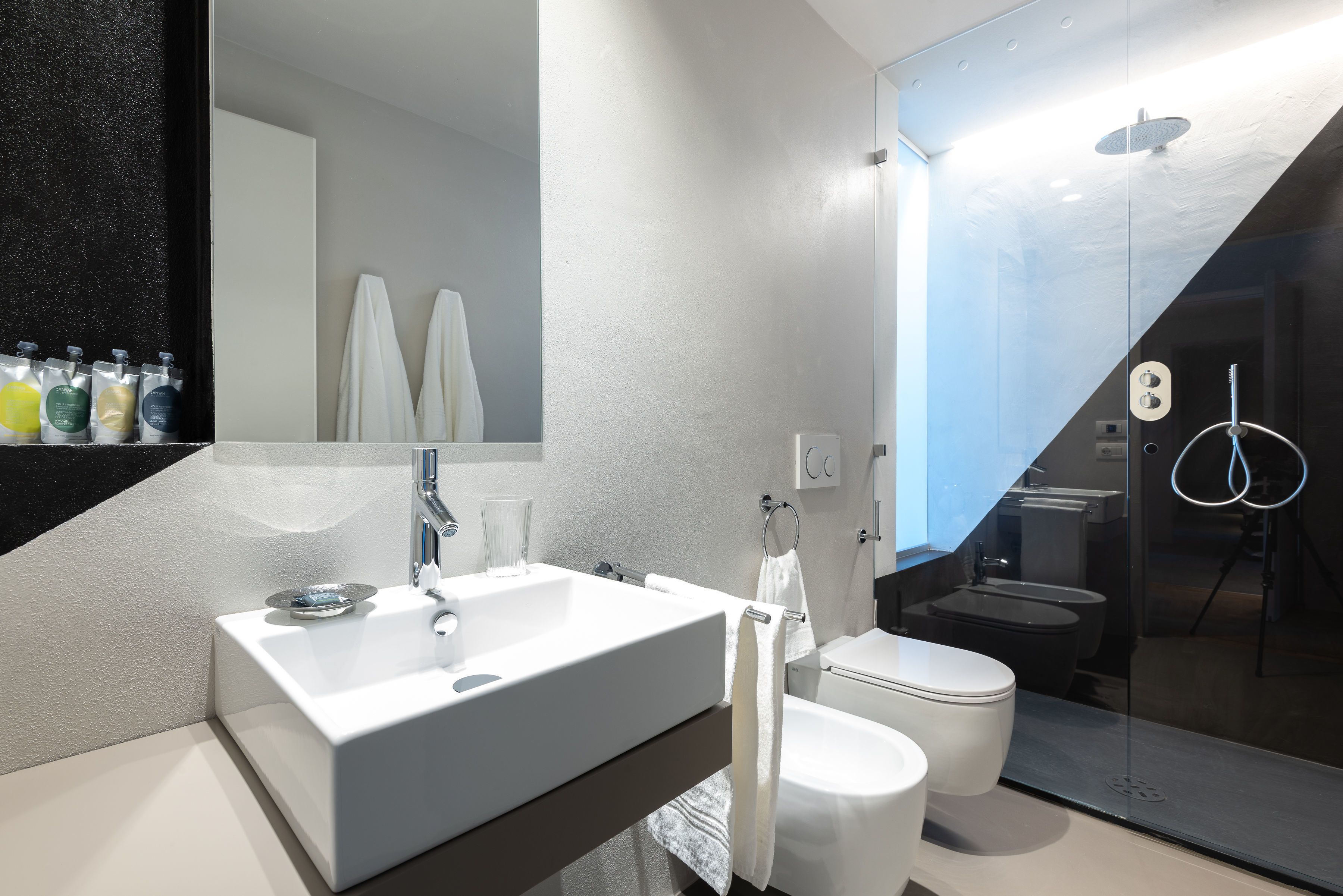 A modern bathroom with a white sink, mirror, and toilet. There are towels hanging on the wall and a glass shower enclosure.