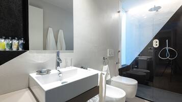 A modern bathroom with a white sink, mirror, and toilet. There are towels hanging on the wall and a glass shower enclosure.