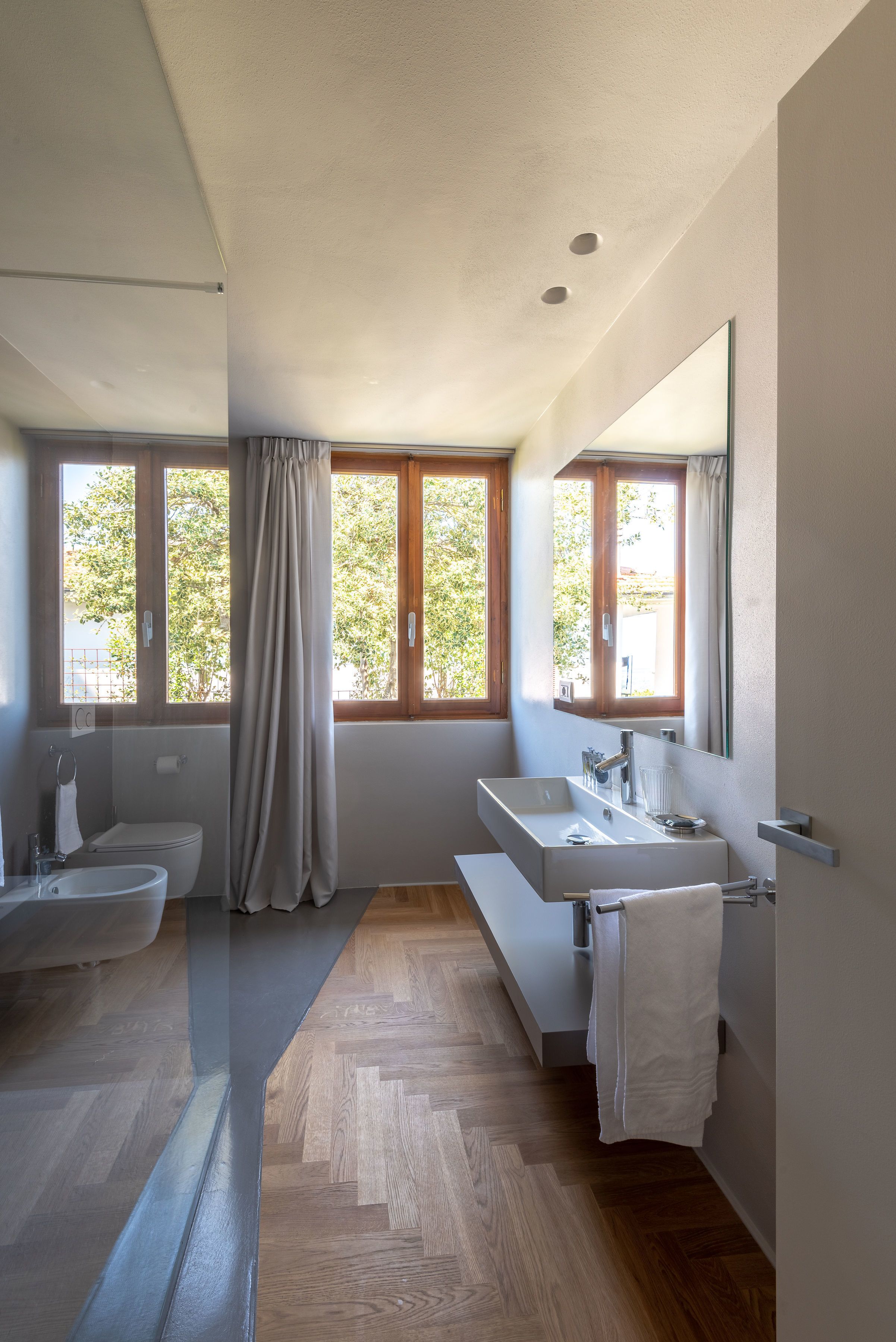 A modern bathroom with a large window, a bidet, a sink, and a mirror.