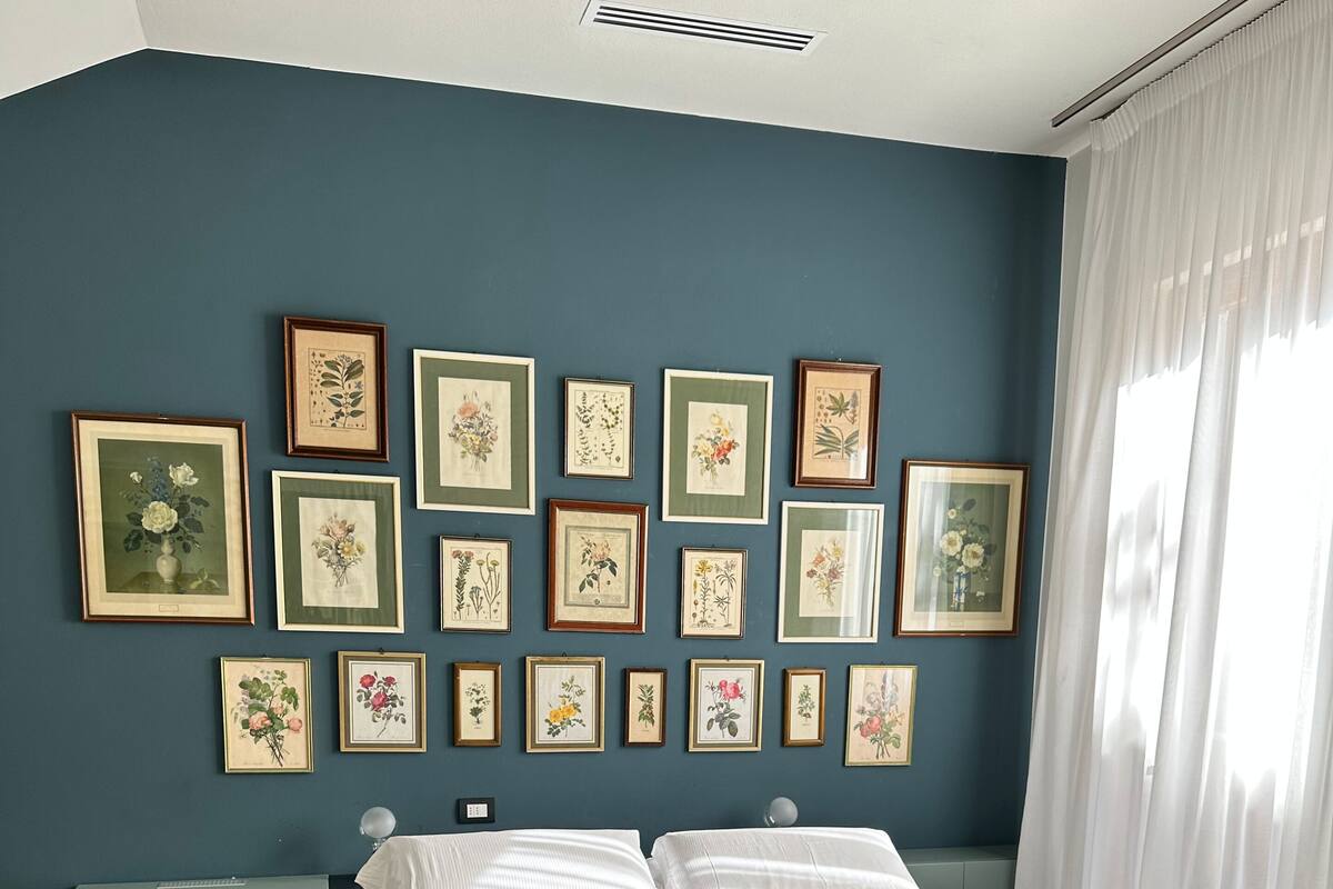 A neatly made bed with white linens and towels, a blue wall with framed botanical prints, and a wooden herringbone floor.