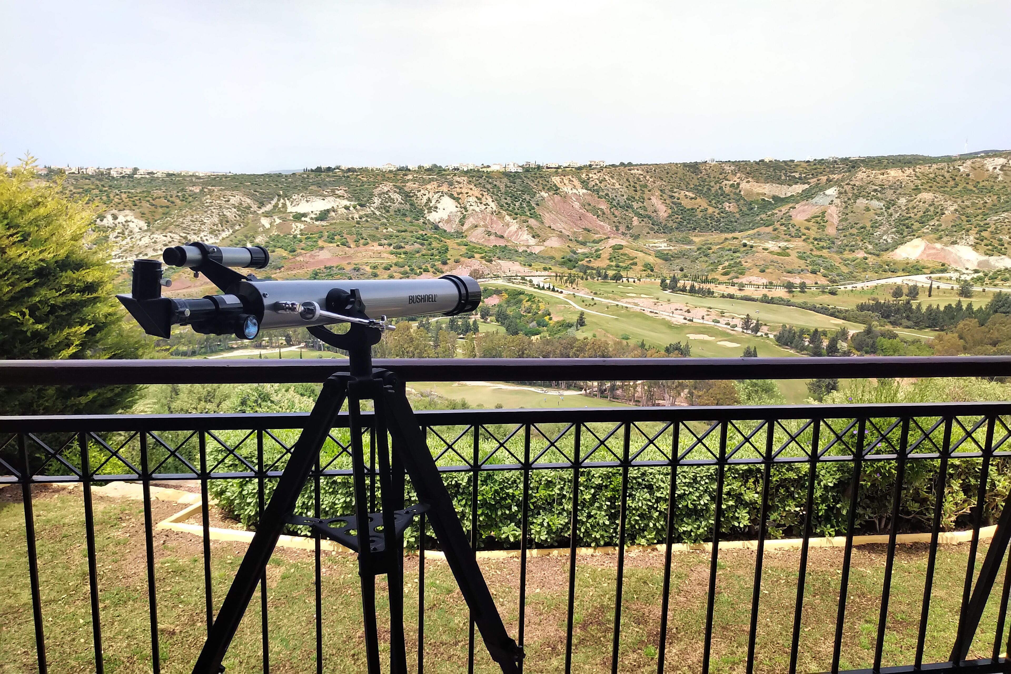 Un télescope est installé sur un balcon qui donne sur un paysage vallonné, avec un terrain de golf en contrebas.