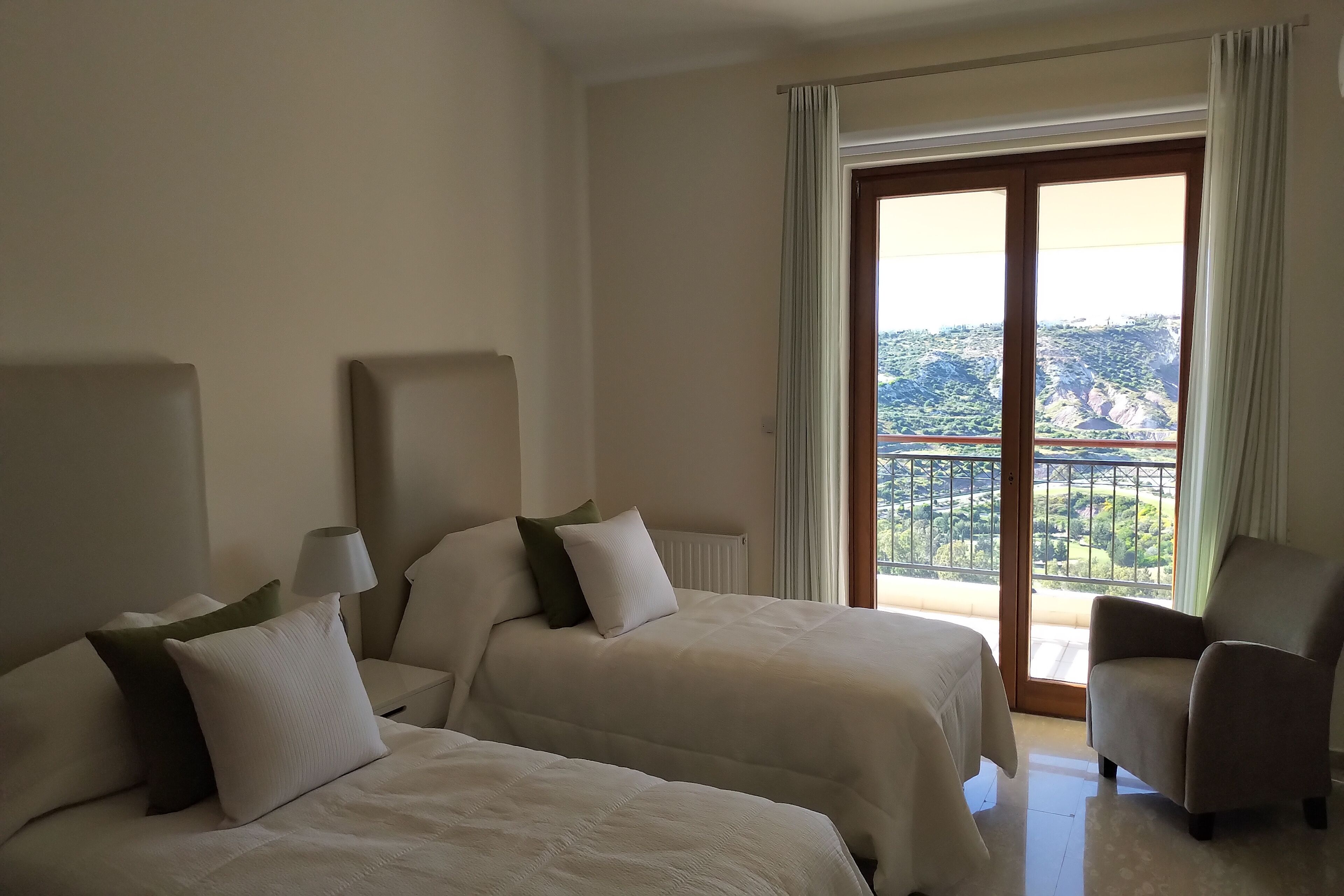 A hotel room with two beds, a chair, and a view of a mountainous landscape through a large window.