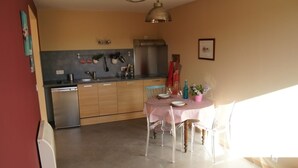 A compact kitchen with a dishwasher, a stainless steel refrigerator, and a dining area with a table set for two. - Studio new condition independent garden, Avignon festival  (ORANGE)