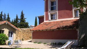 A red building with a stone wall and a tiled roof. There is a white chair and a lounge chair in the front yard. - Studio new condition independent garden, Avignon festival  (ORANGE)
