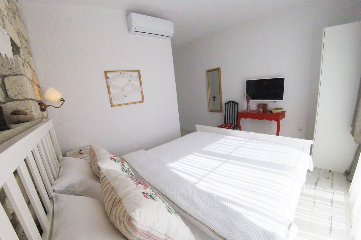 A bedroom with a bed, a television, a mirror, and a stone wall.
