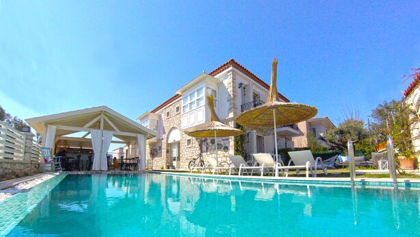 Ein Swimmingpool mit Liegestühlen und Sonnenschirmen, eine überdachte Sitzgelegenheit und ein Steinhaus mit Ziegeldach.